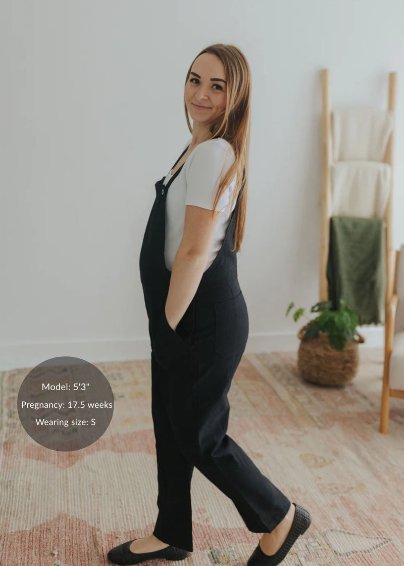 Pregnant woman in black linen/cotton Journey Overalls, size S, with deep pockets and adjustable straps.