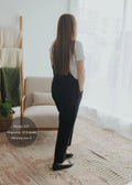 Woman in black linen/cotton Journey Overalls with deep pockets, adjustable straps, and side buttons.