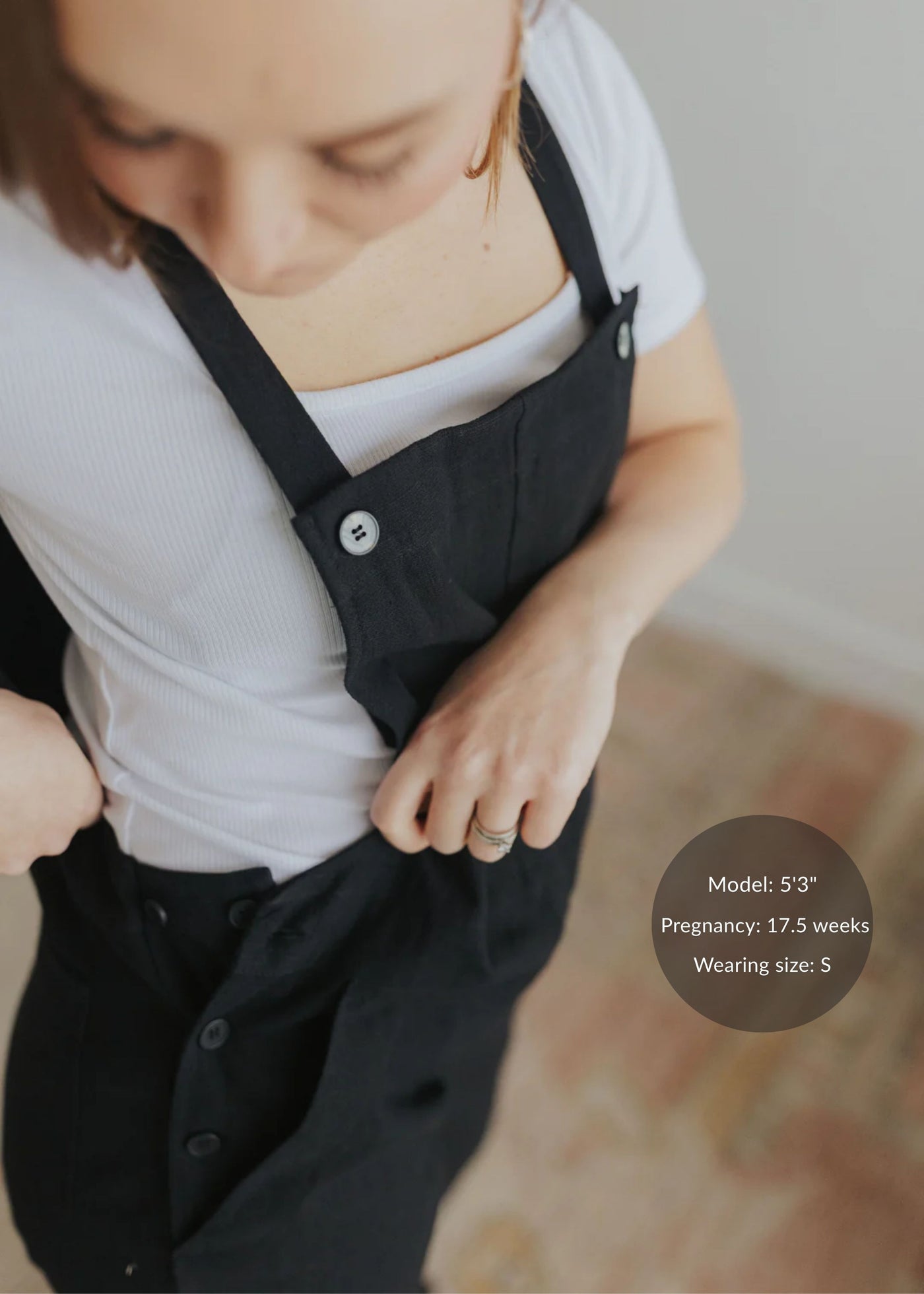 Woman in black linen/cotton overalls with adjustable buttons, worn over a white tee.
