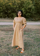 Woman in a flowing, tan lyocell Julia Dress with puff sleeves and pockets, standing outdoors.