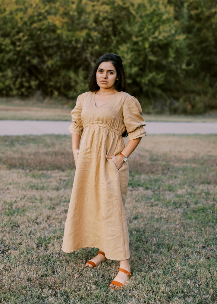 Woman in a flowing, tan lyocell Julia Dress with puff sleeves and pockets, standing outdoors.