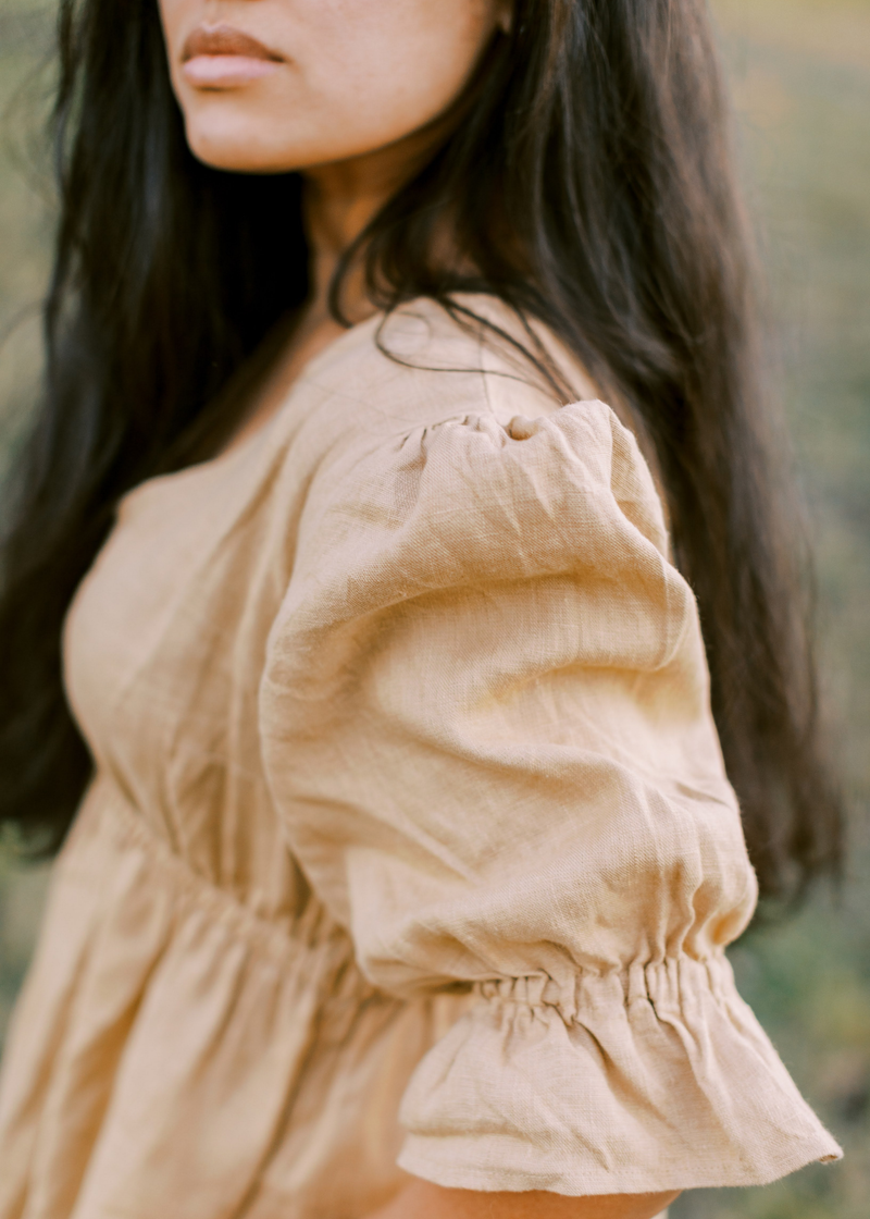 Woman in a beige lyocell Julia Dress with puffed sleeves and a gathered waist.