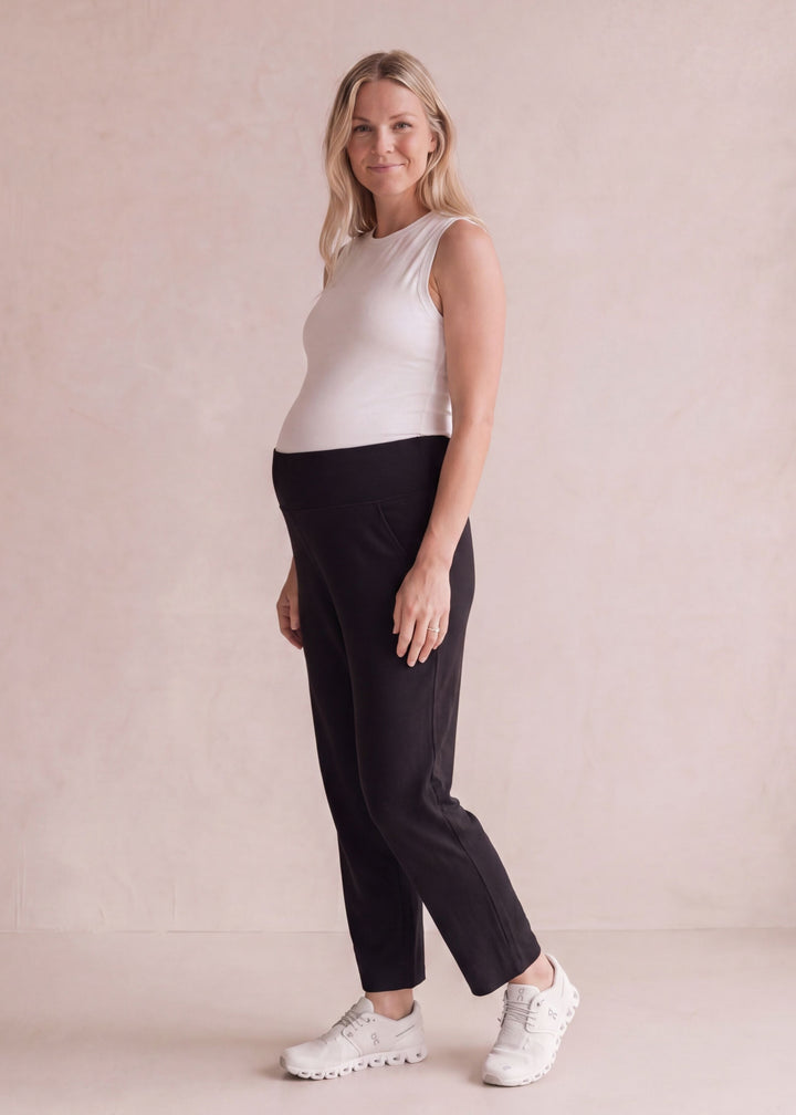 Pregnant woman in black cotton viscose knit sweater pants with a high-rise belly band.