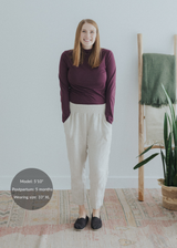 Smiling woman in extended inseam natural linen smocked maternity pants and a plum long-sleeve top.
