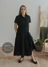 Woman in black cotton poplin Sarah Shirt Dress with short sleeves, button front, and smocked waist.