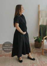 Pregnant woman in a black cotton poplin Sarah Shirt Dress with short sleeves, shirred waist, and full skirt.