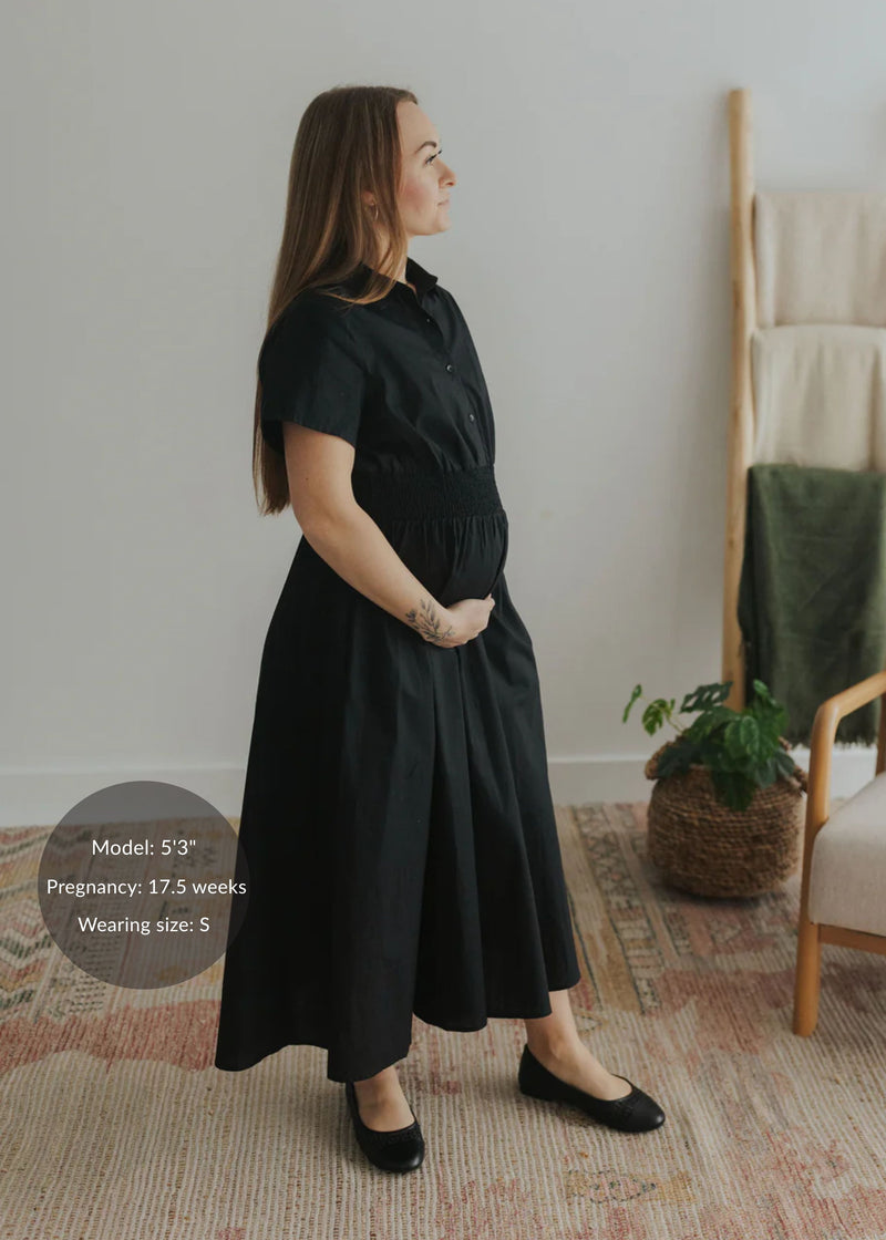 Pregnant woman in a black cotton poplin Sarah Shirt Dress with short sleeves, shirred waist, and full skirt.