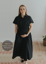 Pregnant woman in a black cotton poplin Sarah Shirt Dress with a relaxed silhouette and smocked waist.