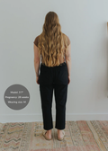 Back view of a pregnant woman wearing black smocked linen maternity pants and a brown top.