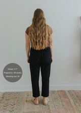 Back view of a pregnant woman wearing black smocked linen maternity pants and a brown top.