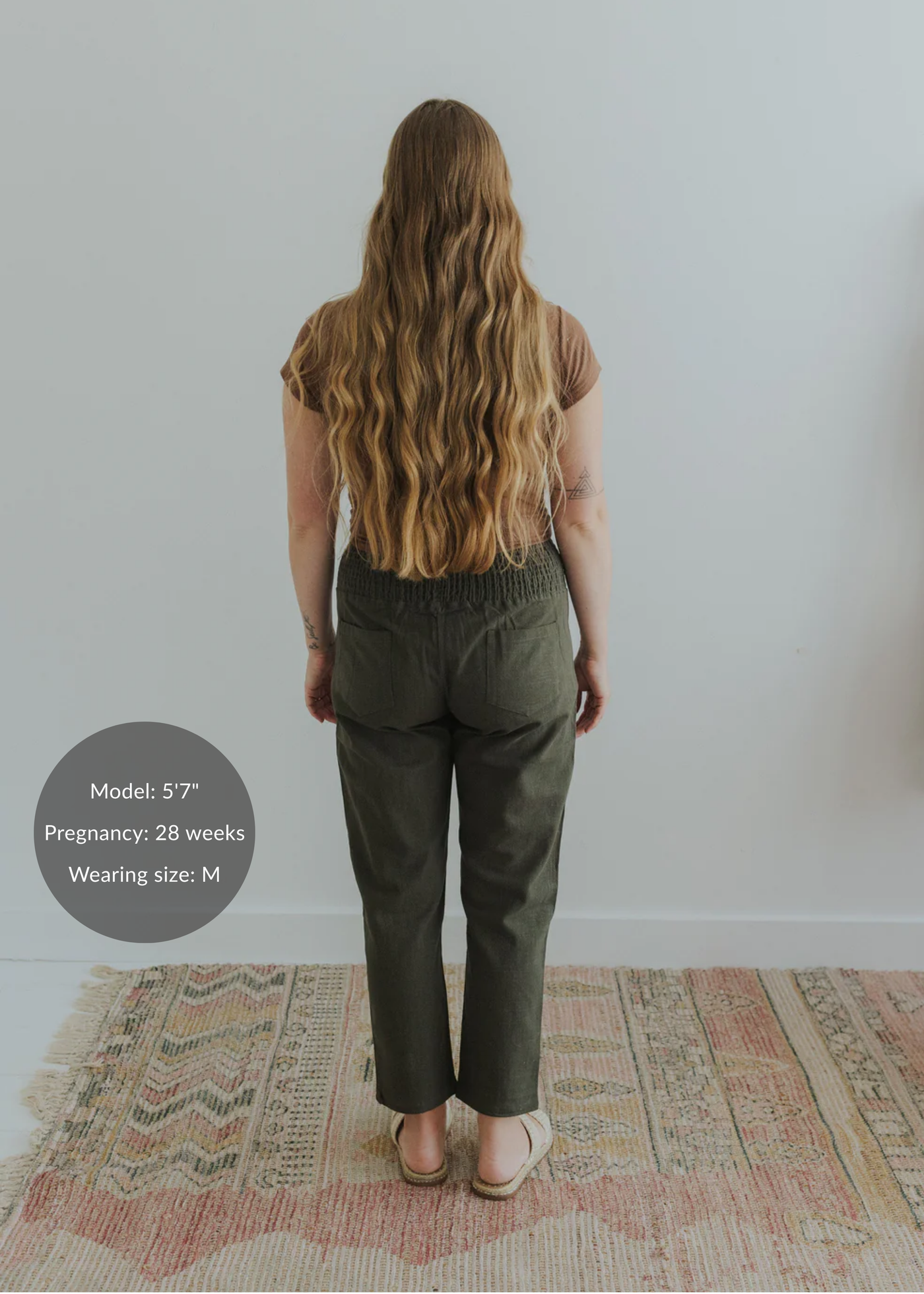 Back view of a pregnant model wearing olive green smocked linen pants with functional pockets.