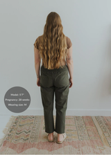 Back view of a pregnant model wearing olive green smocked linen pants with functional pockets.