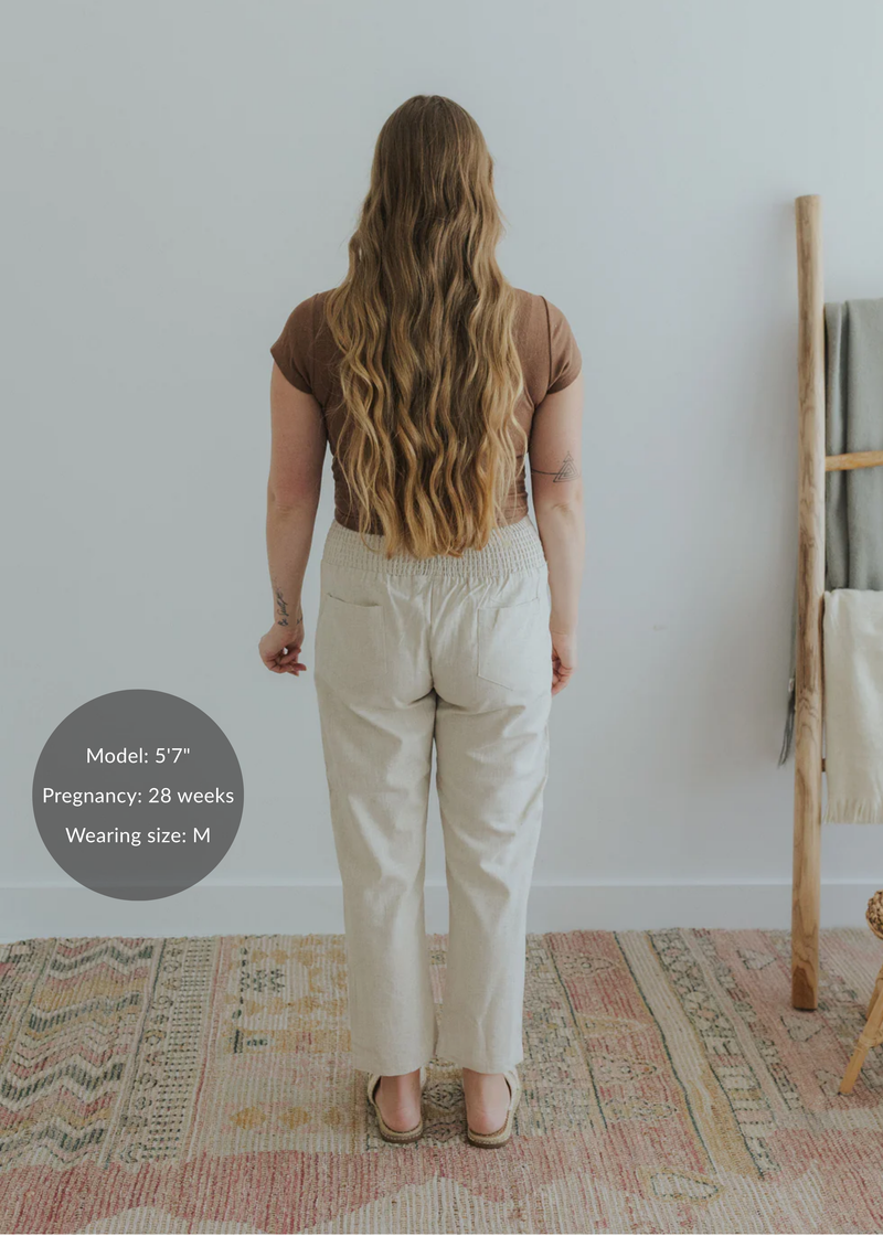 Back view of a pregnant model wearing natural linen smocked waist pants with pockets.
