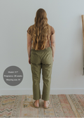 Back view of a pregnant model wearing olive green smocked linen maternity pants with pockets.