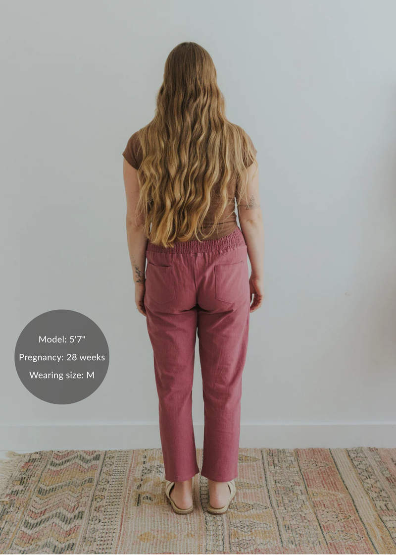 Back view of a pregnant model wearing M-sized, rose-colored smocked linen maternity pants with pockets.