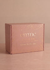 Pink Emme Mystery Box with gold leaf and text, "5 items: $325+ value" on a light wood surface.