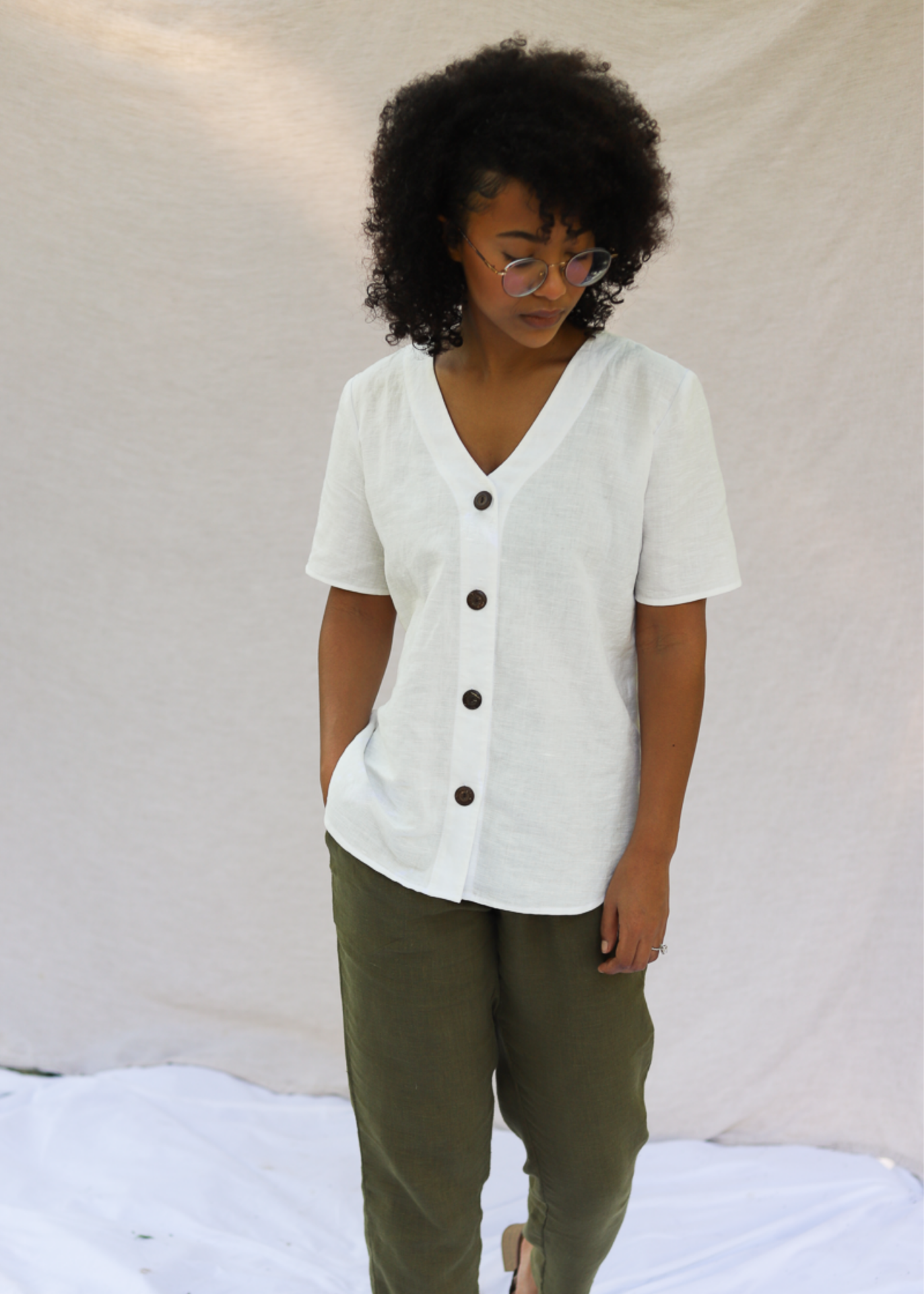 Woman in white linen-cotton Olivia Button Down Top with brown buttons and olive green pants.