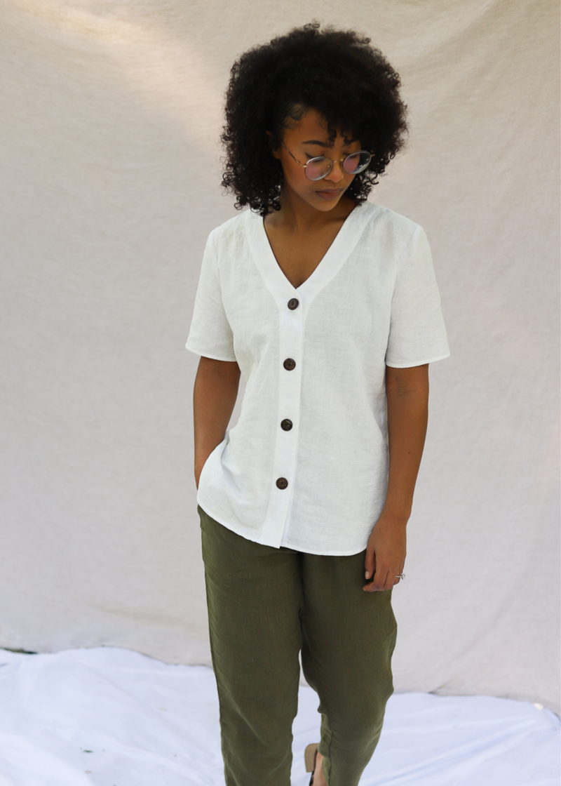 Woman in white linen-cotton Olivia Button Down Top with brown buttons and olive green pants.
