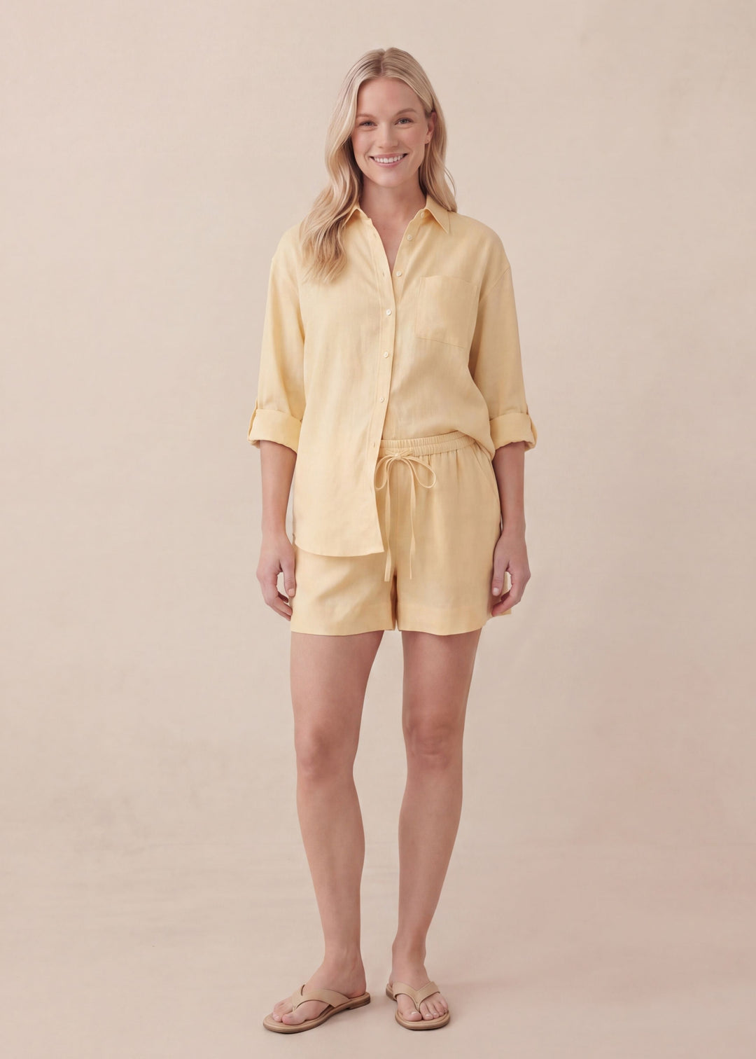 Smiling woman in a yellow oversized linen co-ord with a button-up shirt and drawstring shorts.