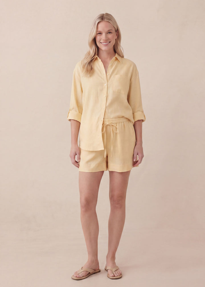 Smiling woman in a yellow oversized linen co-ord with a button-up shirt and drawstring shorts.