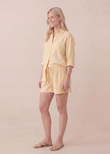 Smiling woman wearing an oversized yellow linen co-ord set with a button-up shirt and drawstring shorts.