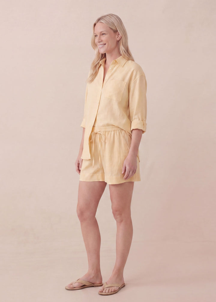 Smiling woman wearing an oversized yellow linen co-ord set with a button-up shirt and drawstring shorts.
