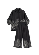 Black oversized cotton smocked set with white floral print, featuring a relaxed shirt and wide-leg pants.