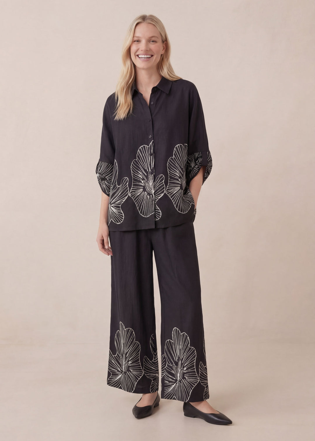 Smiling model in a black oversized cotton smocked set with white floral print, featuring a relaxed shirt and wide-leg pants.
