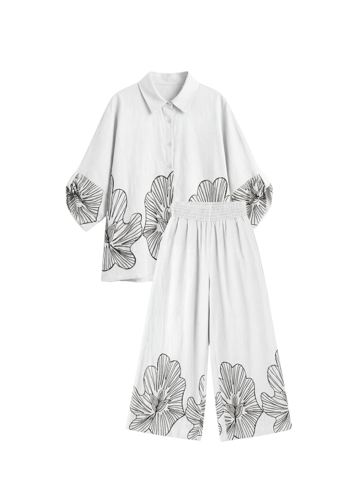 White oversized cotton smocked set with black floral print, featuring a loose shirt and wide-leg pants.
