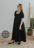 Black cotton gauze maxi dress with square neck, smocked bodice, puffed sleeves, and tiered skirt.