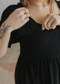 Close-up of a woman in a black cotton gauze square neck dress with smocked bodice and puffed sleeves.