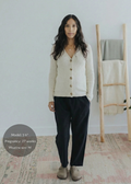 Woman in black cotton/linen straight leg trousers, cream ribbed cardigan, and tan clogs.