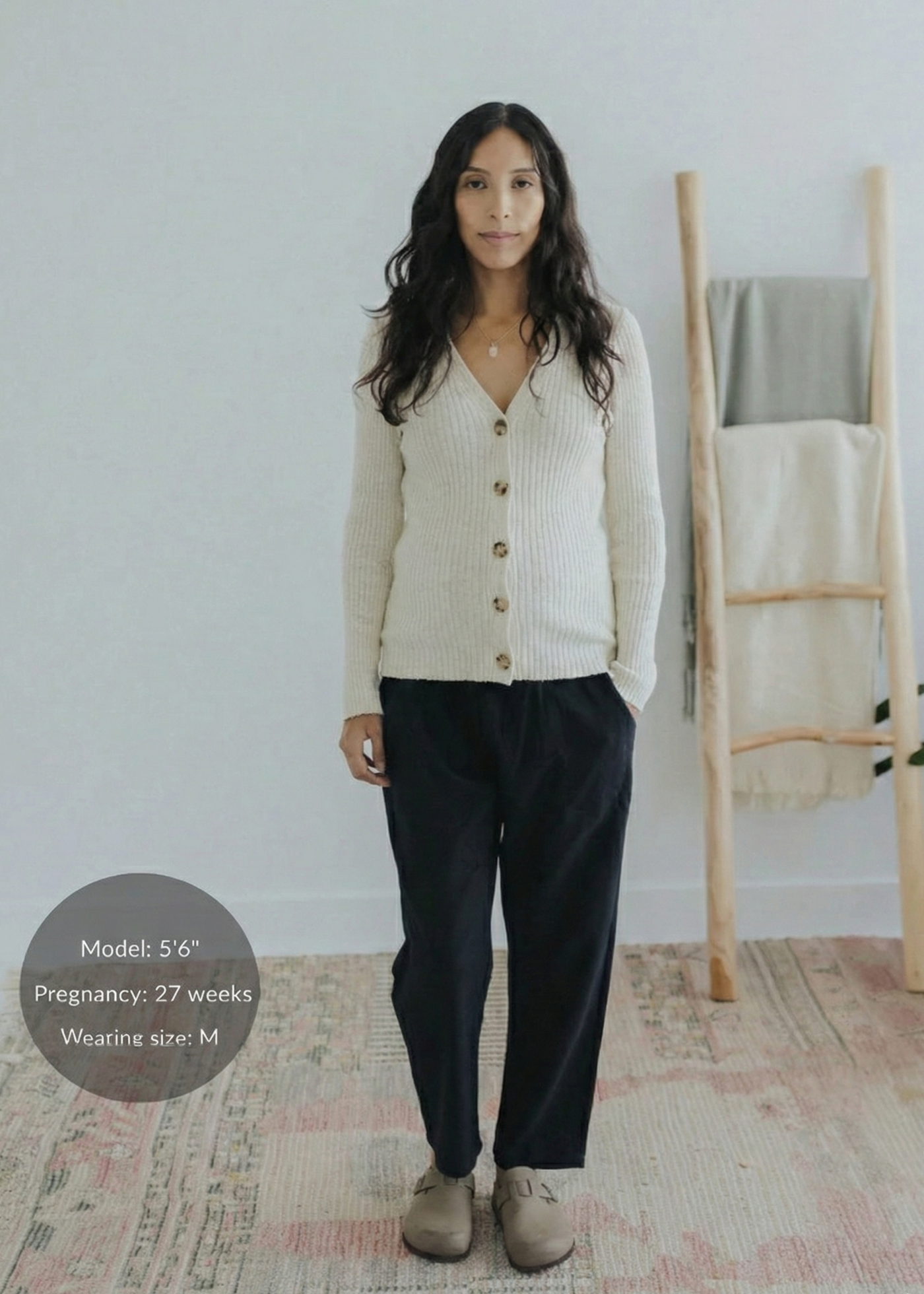 Woman in black cotton/linen straight leg trousers, cream ribbed cardigan, and tan clogs.