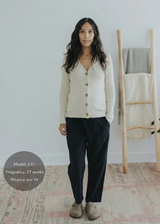 Woman in black cotton/linen straight leg trousers, cream ribbed cardigan, and tan clogs.
