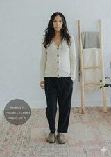 Pregnant woman in black straight-leg cotton/linen trousers, cream cardigan, and taupe clogs.