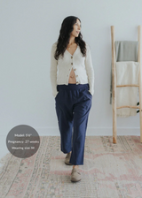 Pregnant woman in navy straight leg cotton/linen trousers with an elastic waist, paired with a cream cardigan.