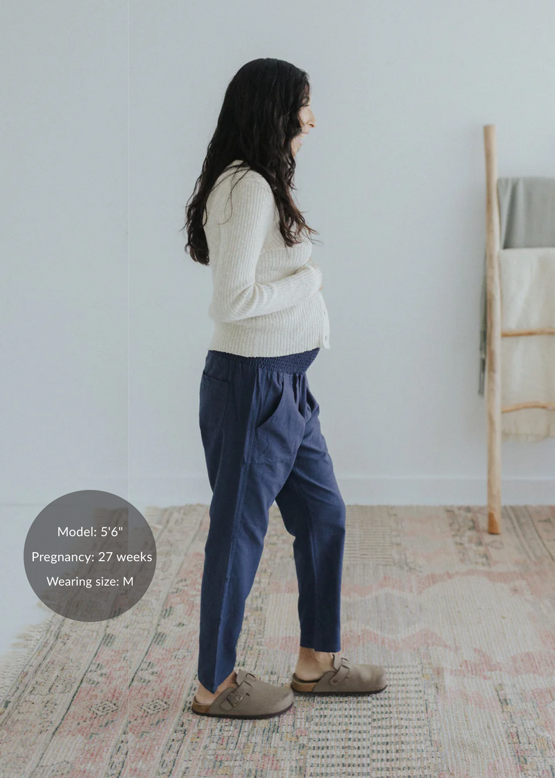 Pregnant model in navy straight-leg cotton/linen trousers with elastic waist and pockets, paired with a cream sweater.