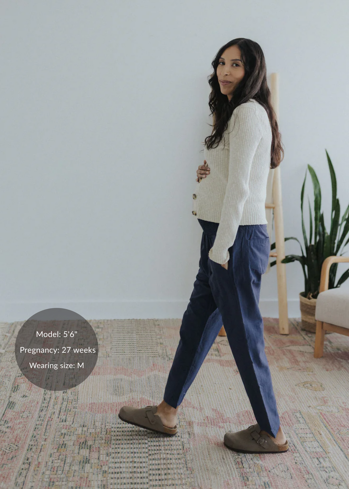 Pregnant model wearing navy straight leg cotton/linen trousers with a cream cardigan and brown mules.