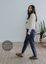 Pregnant model wearing navy straight leg cotton/linen trousers with a cream cardigan and brown mules.