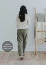 Pregnant model from behind wearing olive straight leg cotton/linen trousers and a cream sweater.