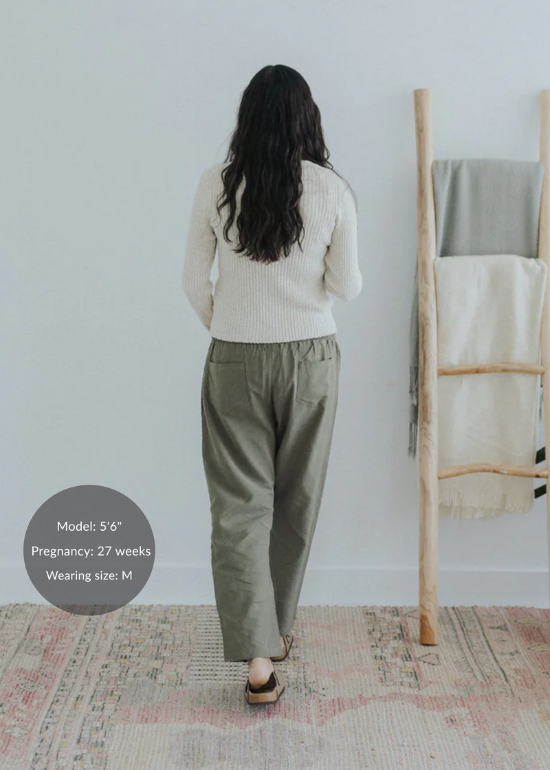 Pregnant model from behind wearing olive straight leg cotton/linen trousers and a cream sweater.