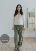 Pregnant woman in olive green straight leg cotton/linen trousers with an elastic waist, paired with a cream cardigan.