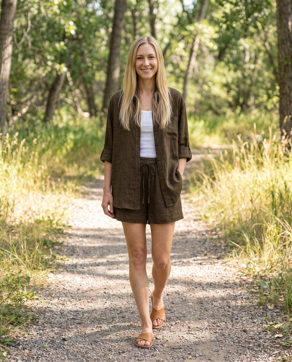 Woman wearing the Sunroom Set in Olive sandwashed linen, shirt open over a white tank, on a wooded trail
