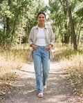 Woman wearing the Sunroom Shirt in Natural sandwashed linen open over a white tank with jeans on a wooded trail