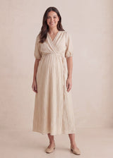 Smiling woman wears a beige textured crossover maternity dress with puff sleeves and a tie waist.