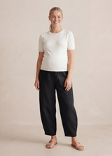 Woman in black linen/cotton barrel pants with a stretchy waistband, deep pockets, and a white top.