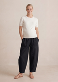Smiling pregnant woman in black linen/cotton barrel pants with deep pockets and a white top.