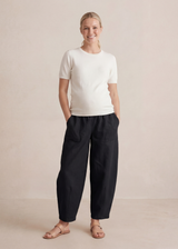 Smiling pregnant woman in black linen/cotton barrel pants with deep pockets and a white top.