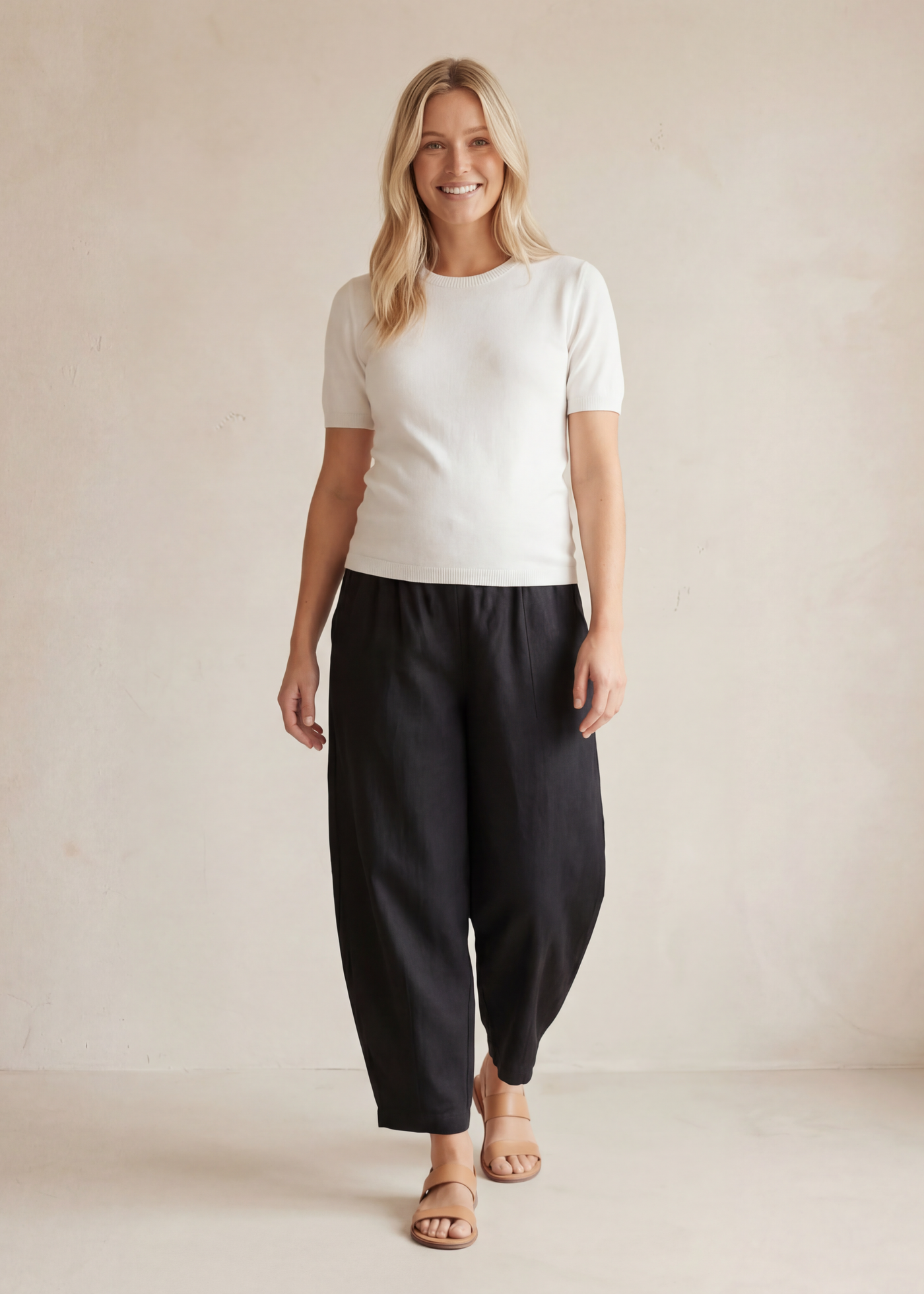 Smiling woman in black linen/cotton barrel pants with deep pockets and a white top.