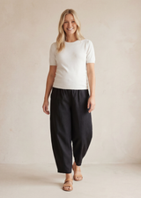 Smiling woman in black linen/cotton barrel pants with deep pockets and a white top.